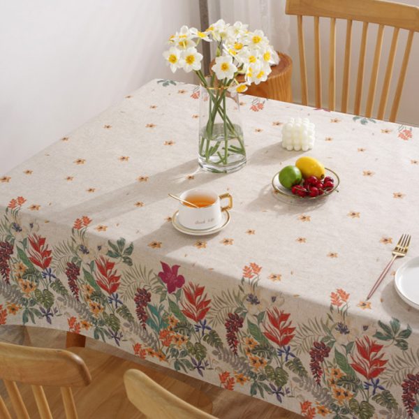 Colorful floral polyester-linen tablecloth with vintage botanical pattern on a light background, styled on a rustic dining table with glassware and wooden chairs.