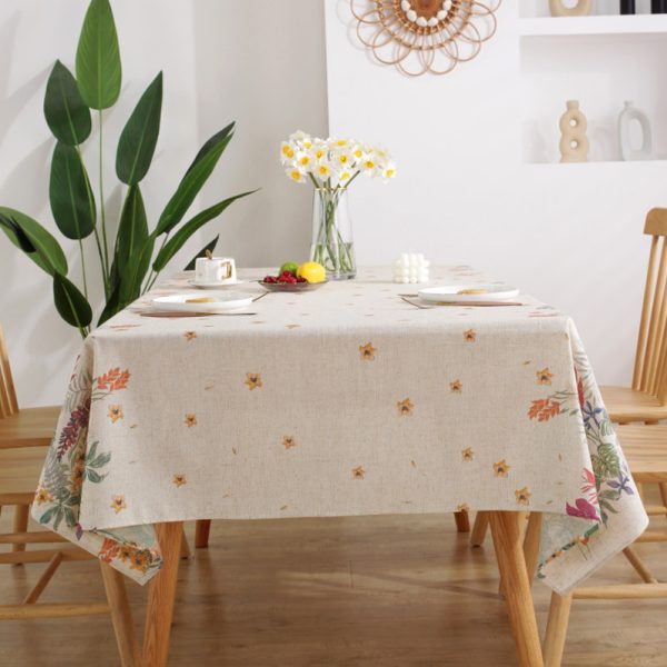 Colorful floral polyester-linen tablecloth with vintage botanical pattern on a light background, styled on a rustic dining table with glassware and wooden chairs.