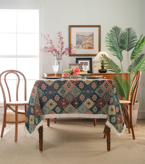 Colorful geometric boho tablecloth with tassel fringe, laid over a rustic dining table with eclectic tableware.