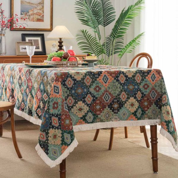 Colorful geometric boho tablecloth with tassel fringe, laid over a rustic dining table with eclectic tableware.