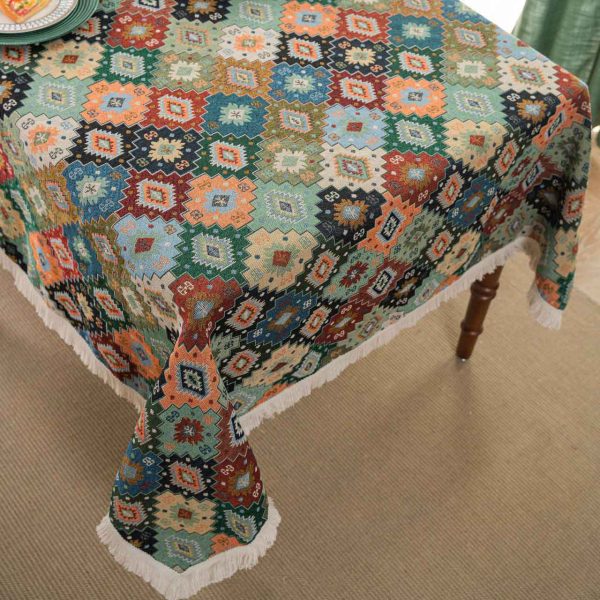Colorful geometric boho tablecloth with tassel fringe, laid over a rustic dining table with eclectic tableware.