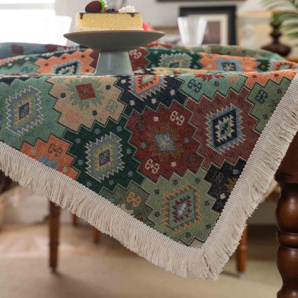 Colorful geometric boho tablecloth with tassel fringe, laid over a rustic dining table with eclectic tableware.