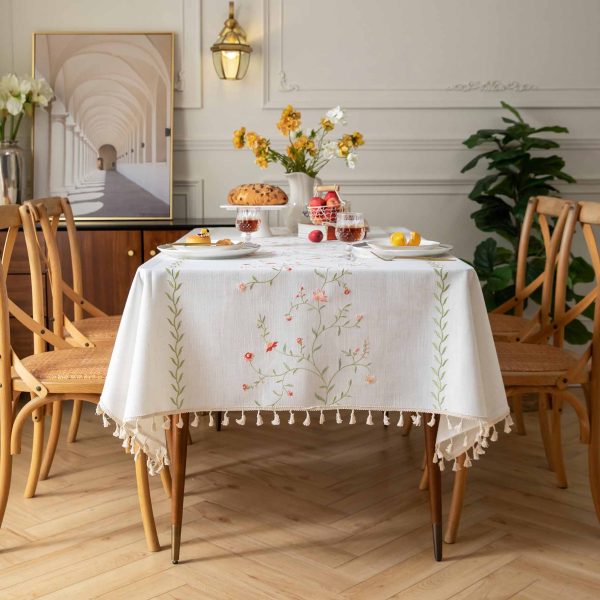 Pink floral faux linen tablecloth with fringe edges on a wooden dining table
