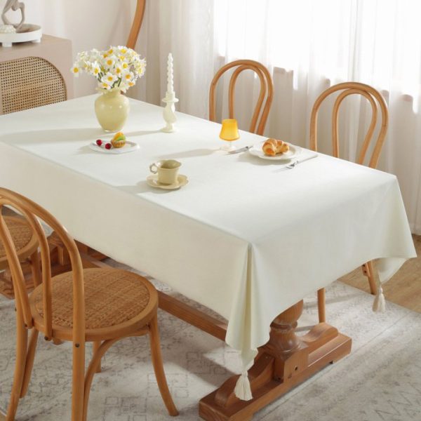 Beige faux linen tablecloth with fringe edges on wooden dining table