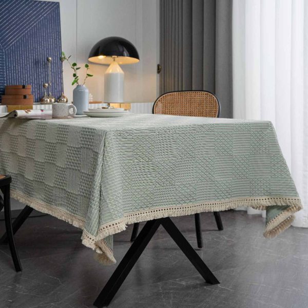 Light green geometric cotton blend tablecloth with tassel trim, styled on rustic and modern dining tables. Features include textured weave, soft fringe edges, and versatile use in kitchens and dining rooms.