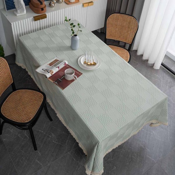 Light green geometric cotton blend tablecloth with tassel trim, styled on rustic and modern dining tables. Features include textured weave, soft fringe edges, and versatile use in kitchens and dining rooms.