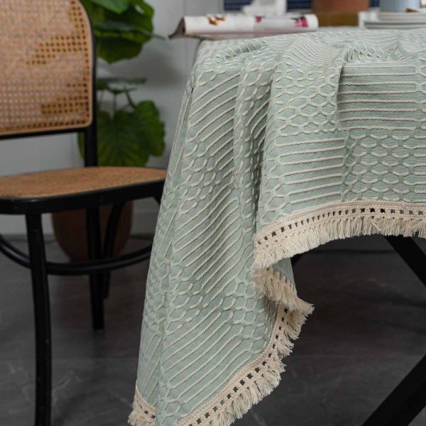 Light green geometric cotton blend tablecloth with tassel trim, styled on rustic and modern dining tables. Features include textured weave, soft fringe edges, and versatile use in kitchens and dining rooms.