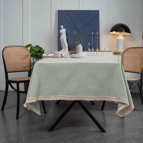Light green geometric cotton blend tablecloth with tassel trim, styled on rustic and modern dining tables. Features include textured weave, soft fringe edges, and versatile use in kitchens and dining rooms.