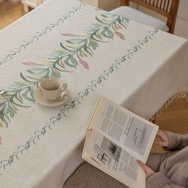 Beige faux linen tablecloth with brown embroidered leaf pattern and tassel fringe, made from polyester-linen blend, suitable for dining tables or outdoor settings.