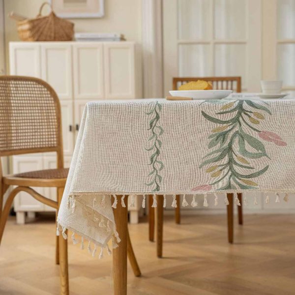 Beige faux linen tablecloth with brown embroidered leaf pattern and tassel fringe, made from polyester-linen blend, suitable for dining tables or outdoor settings.