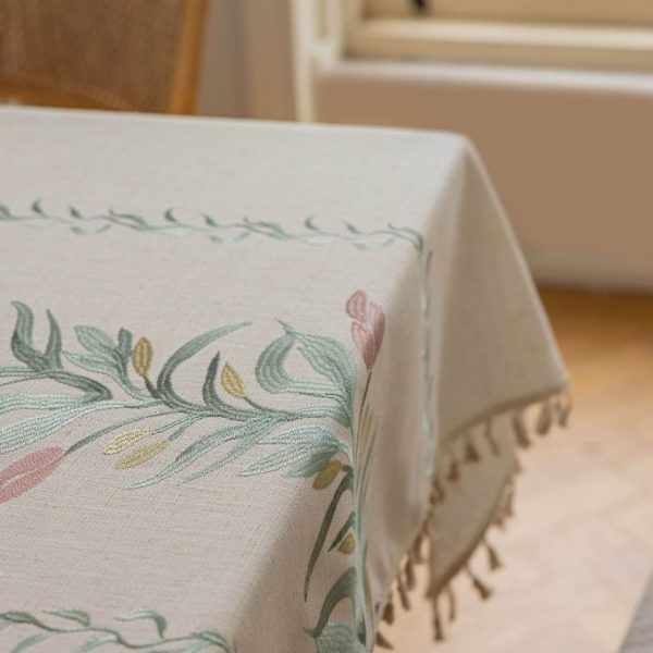 Beige faux linen tablecloth with brown embroidered leaf pattern and tassel fringe, made from polyester-linen blend, suitable for dining tables or outdoor settings.