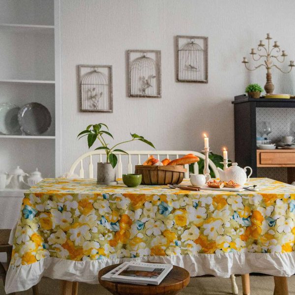 Yellow floral cotton tablecloth with white ruffled trim, styled on a rustic table for spring or cottagecore dining. Features soft fabric, bright flower print, and elegant edge detail.