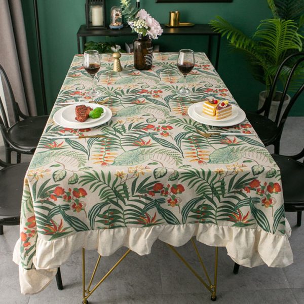 Tropical cotton-linen tablecloth with green palm and floral print, ruffled edge, styled in a light rustic dining setup.