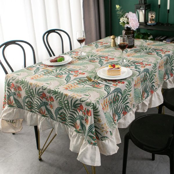 Tropical cotton-linen tablecloth with green palm and floral print, ruffled edge, styled in a light rustic dining setup.