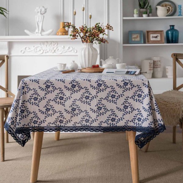 A hand-painted blue vine floral cotton linen tablecloth with navy lace trim, styled on a rustic wooden table with minimalist dinnerware and greenery.
