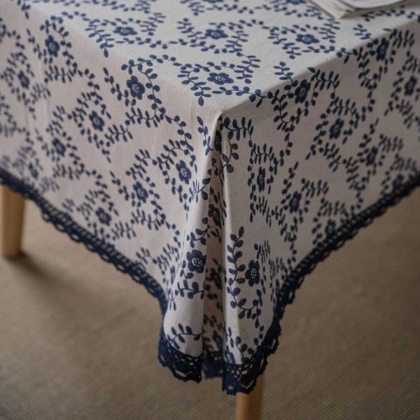 A hand-painted blue vine floral cotton linen tablecloth with navy lace trim, styled on a rustic wooden table with minimalist dinnerware and greenery.