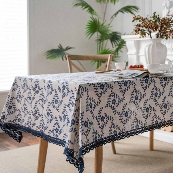 A hand-painted blue vine floral cotton linen tablecloth with navy lace trim, styled on a rustic wooden table with minimalist dinnerware and greenery.
