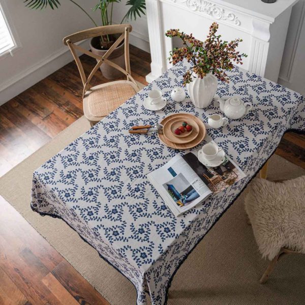 A hand-painted blue vine floral cotton linen tablecloth with navy lace trim, styled on a rustic wooden table with minimalist dinnerware and greenery.