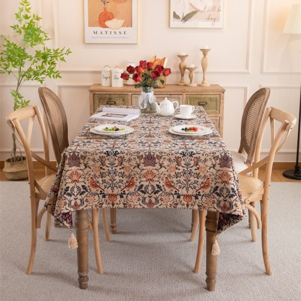 Vintage-style tablecloth featuring colorful floral and bird patterns, woven in a cotton-blend fabric with elegant tassel trim, perfect for farmhouse or cottage-style dining settings.