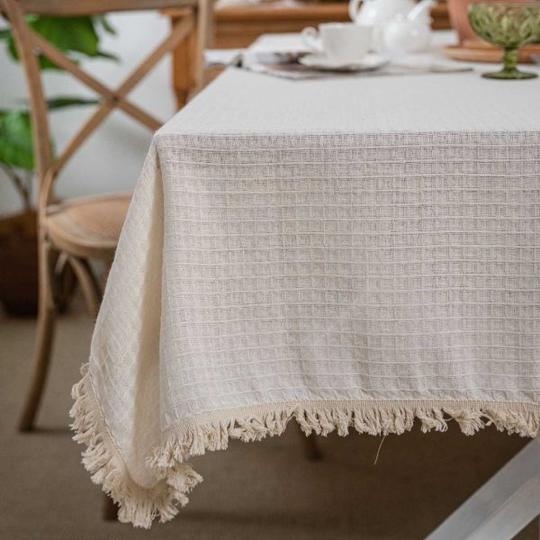 Beige waffle weave cotton-poly tablecloth with tassels, perfect for rustic or minimalist dining decor.