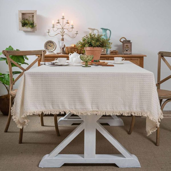 Beige waffle weave cotton-poly tablecloth with tassels, perfect for rustic or minimalist dining decor.