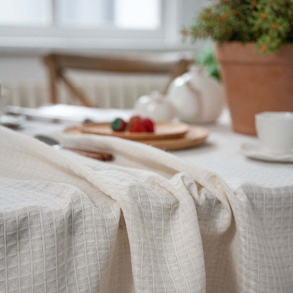 Beige waffle weave cotton-poly tablecloth with tassels, perfect for rustic or minimalist dining decor.