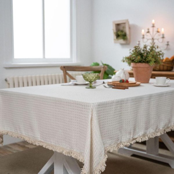 Beige waffle weave cotton-poly tablecloth with tassels, perfect for rustic or minimalist dining decor.