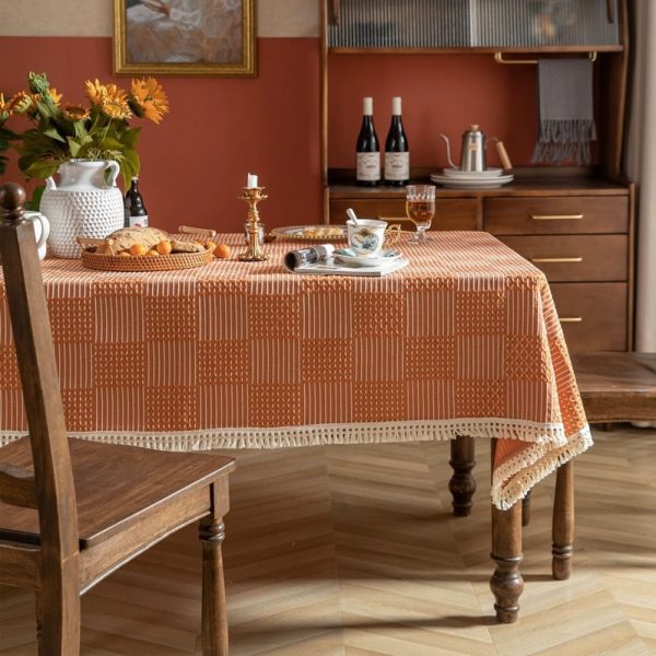 Modern orange plaid polyester tablecloth with white tassel fringe, styled in a bright dining room setting.