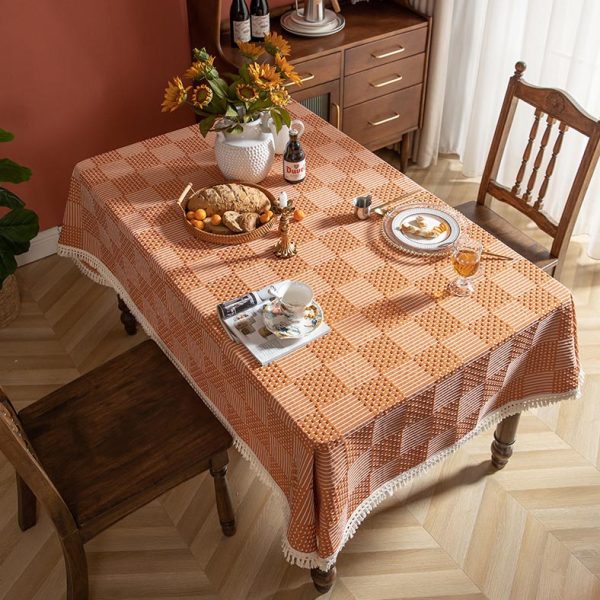Modern orange plaid polyester tablecloth with white tassel fringe, styled in a bright dining room setting.