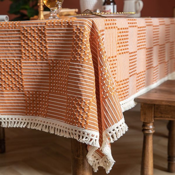Modern orange plaid polyester tablecloth with white tassel fringe, styled in a bright dining room setting.