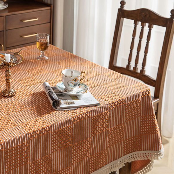 Modern orange plaid polyester tablecloth with white tassel fringe, styled in a bright dining room setting.