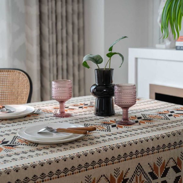 Rustic brown jacquard tablecloth with snowflake pattern and tassel fringe, draped over a wooden dining table in a cozy bohemian-style room.
