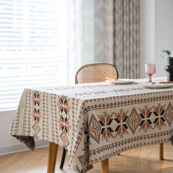 Rustic brown jacquard tablecloth with snowflake pattern and tassel fringe, draped over a wooden dining table in a cozy bohemian-style room.