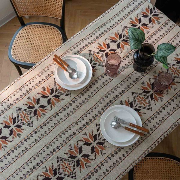 Rustic brown jacquard tablecloth with snowflake pattern and tassel fringe, draped over a wooden dining table in a cozy bohemian-style room.