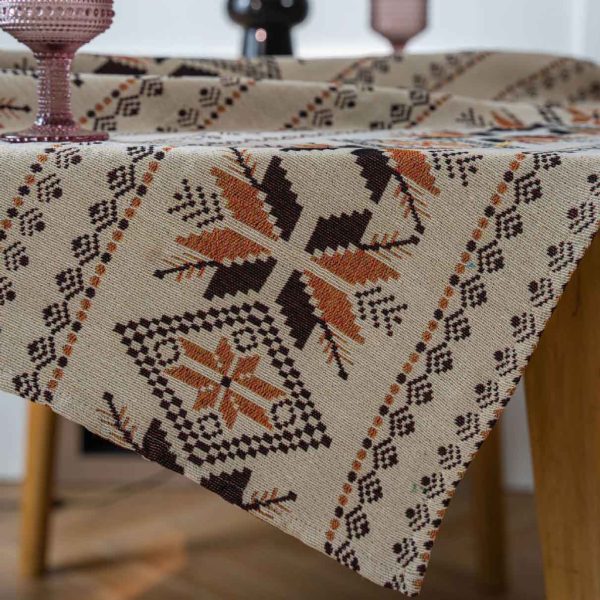 Rustic brown jacquard tablecloth with snowflake pattern and tassel fringe, draped over a wooden dining table in a cozy bohemian-style room.