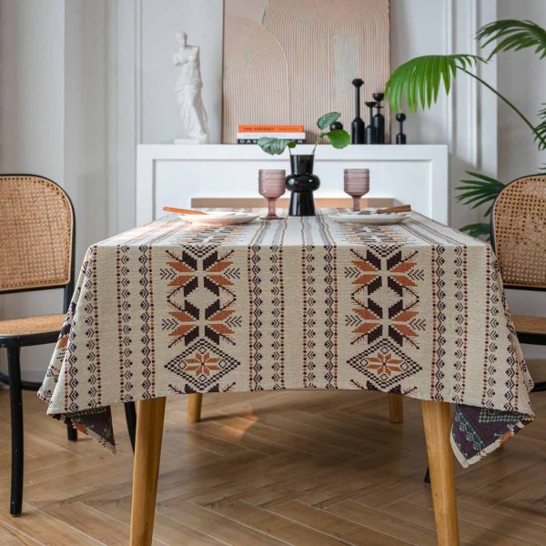 Rustic brown jacquard tablecloth with snowflake pattern and tassel fringe, draped over a wooden dining table in a cozy bohemian-style room.