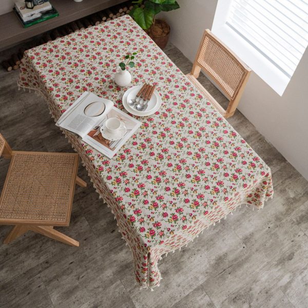 Floral tablecloth with red rose pattern and tassel edges on a rustic wooden table