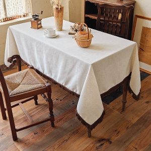 Beige cotton linen tablecloth with tassels on wooden table
