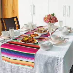 Colorful Mexican table runner with rainbow stripes and tassels on wooden table